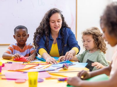 Happy Latin American preschool teacher helping children while doing crafts in class - education concepts